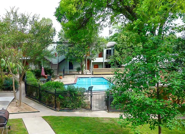 Wide view of the apartment pool courtyard surrounded by trees, walkways, and residential buildings.
