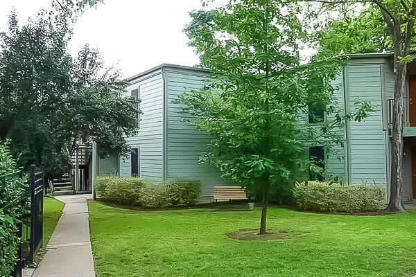 Exterior view of the apartment community with lawn, trees, sidewalk, and two-story buildings.