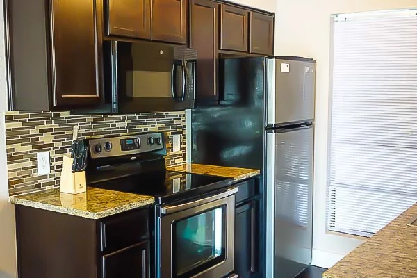 Shared apartment kitchen with dark wood cabinets, granite countertops, stainless steel stove, microwave, and refrigerator.