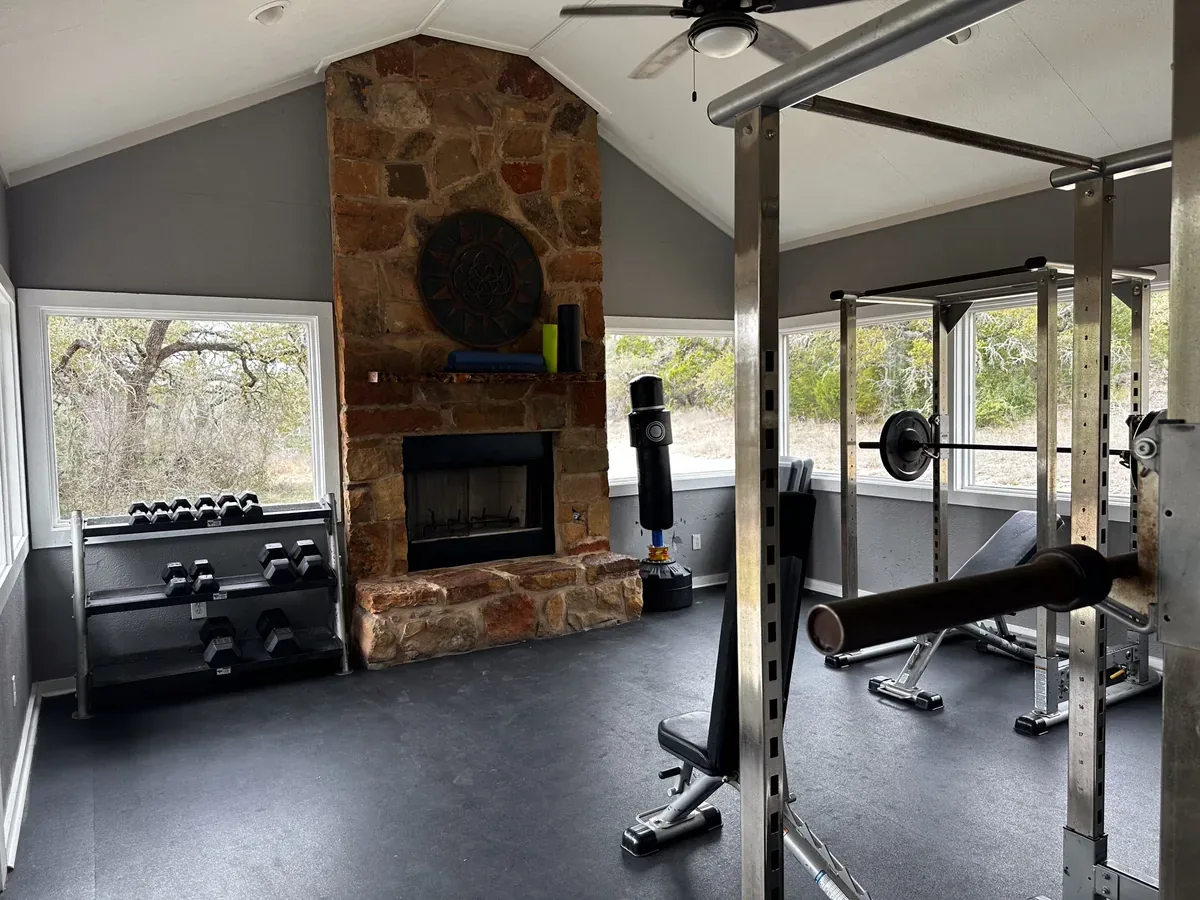 Workout studio with weights and stone fireplace overlooking the Texas Hill Country at Nova Recovery Center.