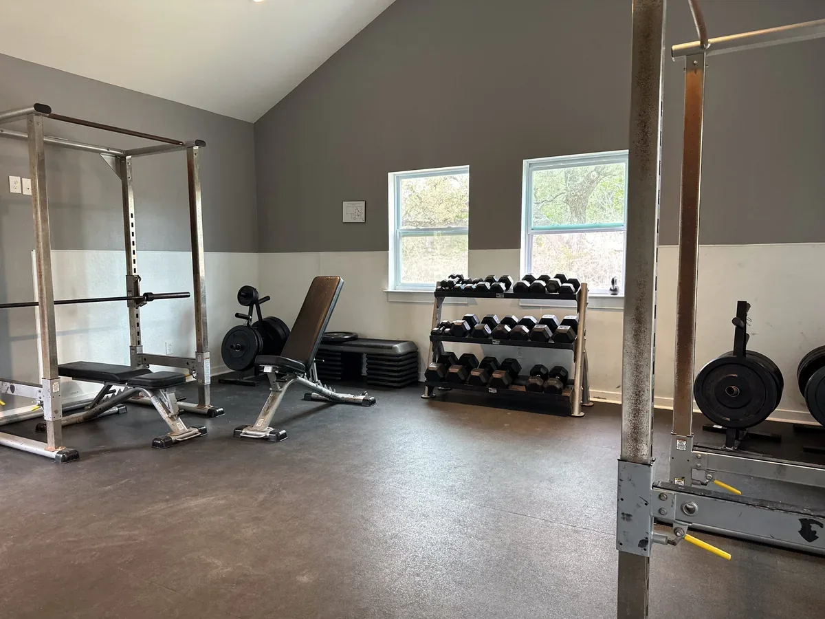 Strength-training room with squat rack, bench, and dumbbells at Nova Recovery Center.