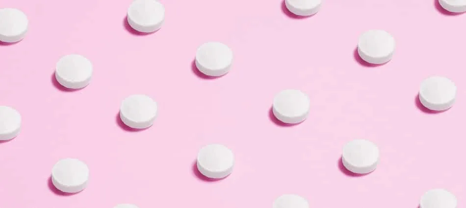 White round tablets arranged in a pattern on a pink background