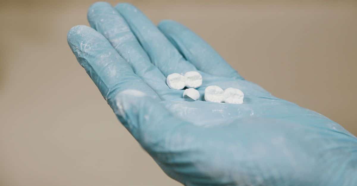 White artificial teeth for denture placed on hand in blue latex glove against light blurred background