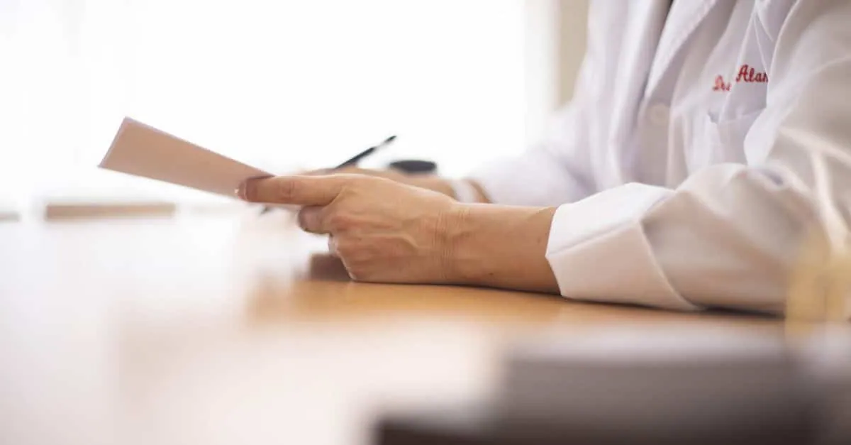 Close-up of a doctor in a lab coat reviewing paperwork at a desk.