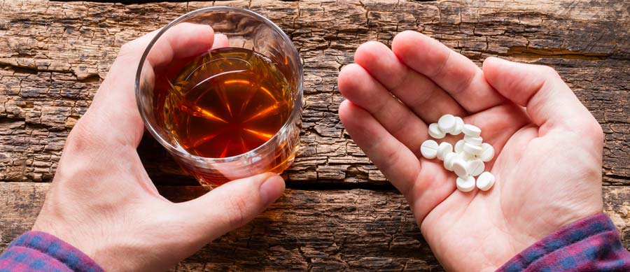 man holds ambien pills and a glass of alcohol