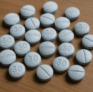 Close-up of multiple blue oxycodone 30 mg tablets scattered on a wooden surface.