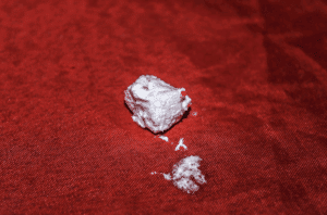 A piece of white powdered substance resembling heroin on a red surface, illustrating its composition and form.