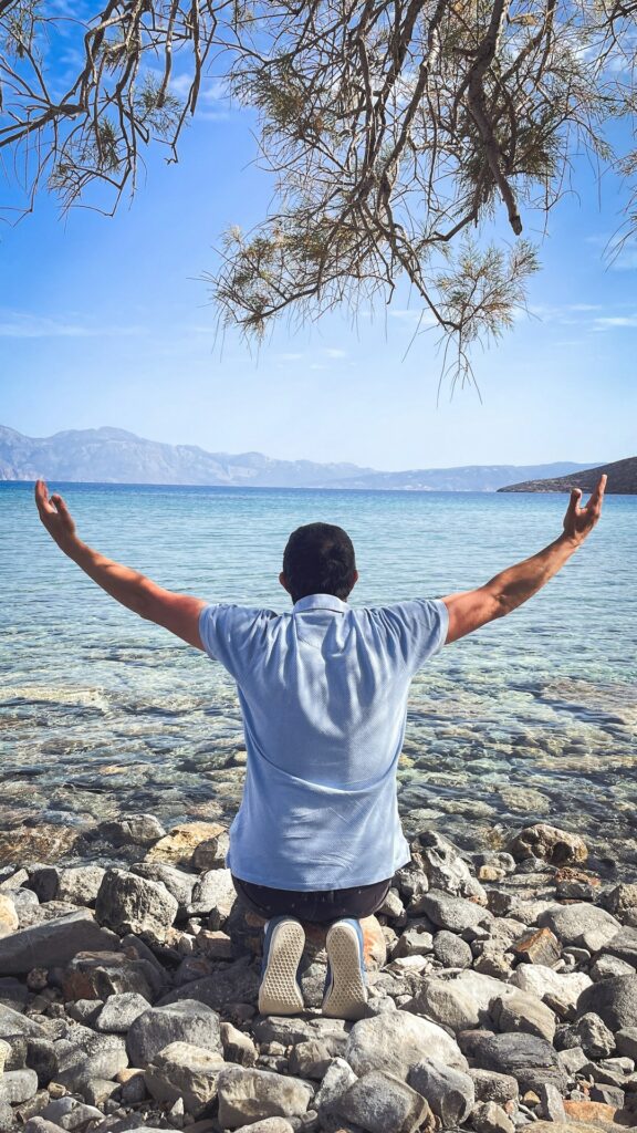 Man kneeling with arms raised towards the sea. -- Photo by Jametlene Reskp on Unsplash