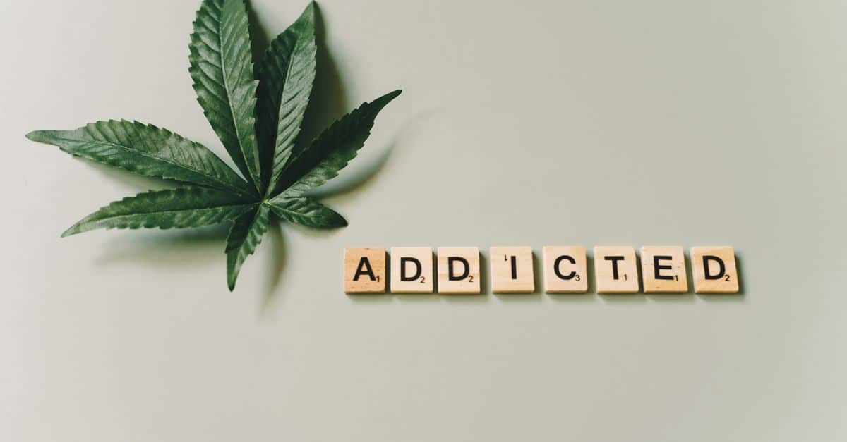 A cannabis leaf and wooden letter tiles spelling 'addicted' on a green surface.
