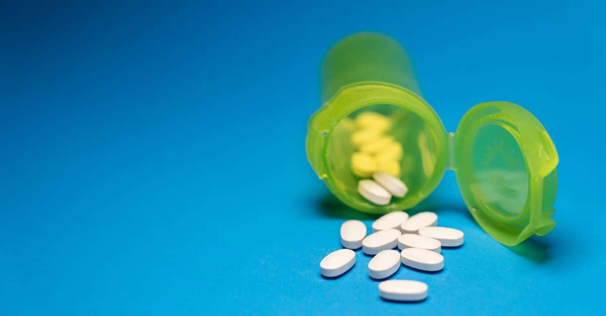 Image of a green pill bottle with white tablets scattered on a blue background, symbolizing healthcare and medication.