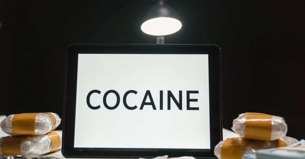 Tablet computer displaying the word 'Cocaine' surrounded by wrapped packets in a dimly lit setting.
