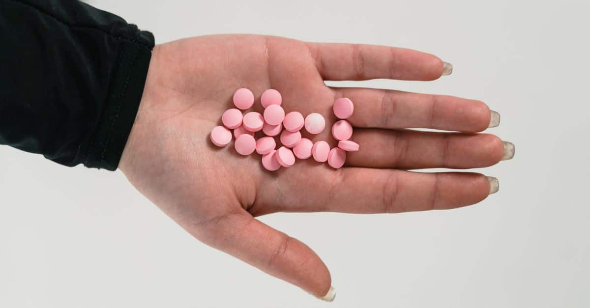 A close-up of a hand holding pink pills, highlighting addiction and healthcare themes.