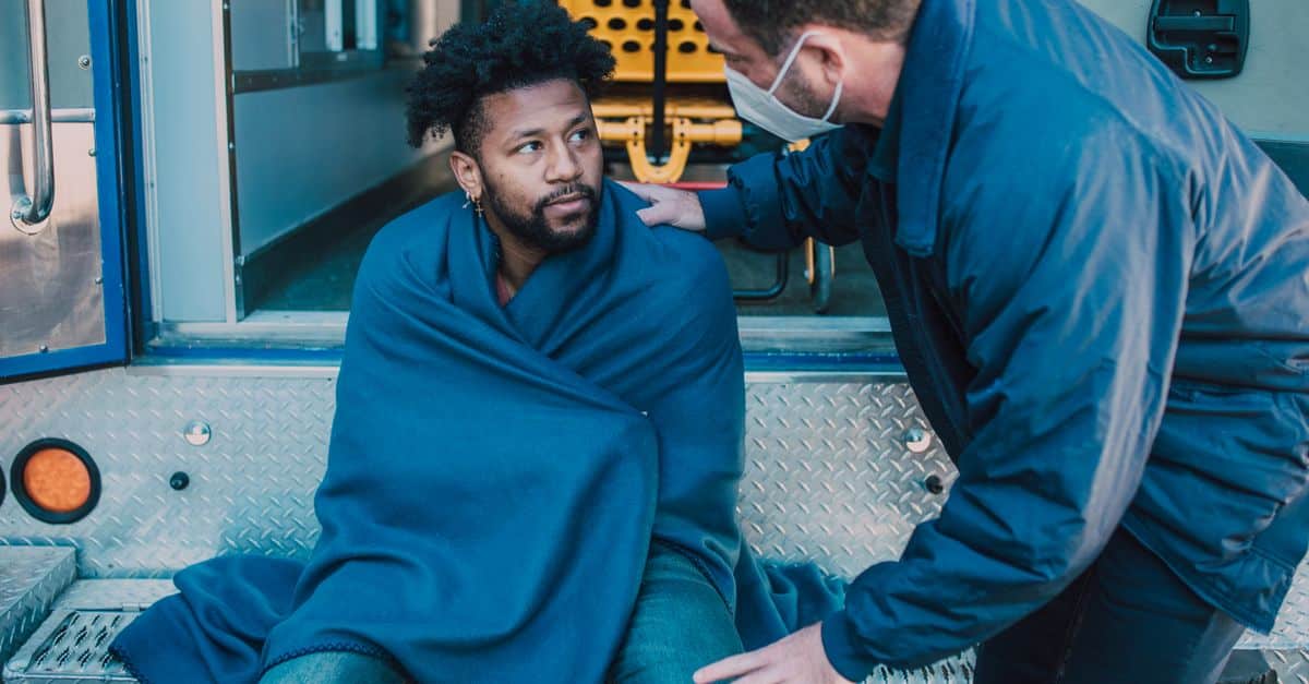 EMTs assist a man wrapped in a blanket near an ambulance, emphasizing care and response.
