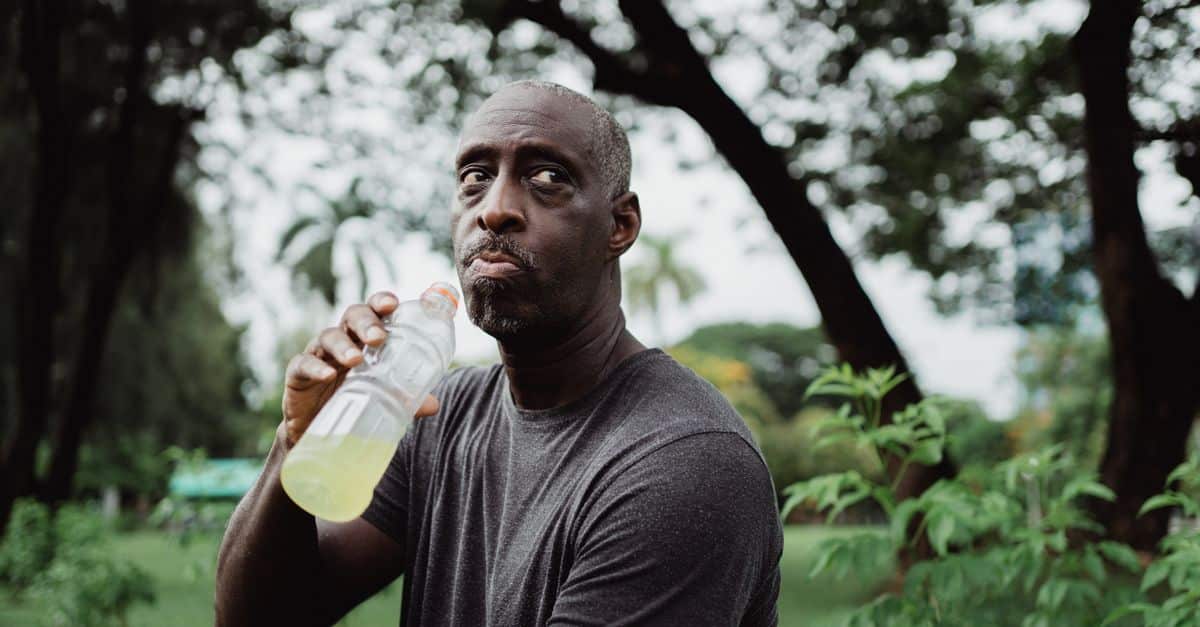 An adult man drinking from a bottle in a lush green park, staying hydrated.