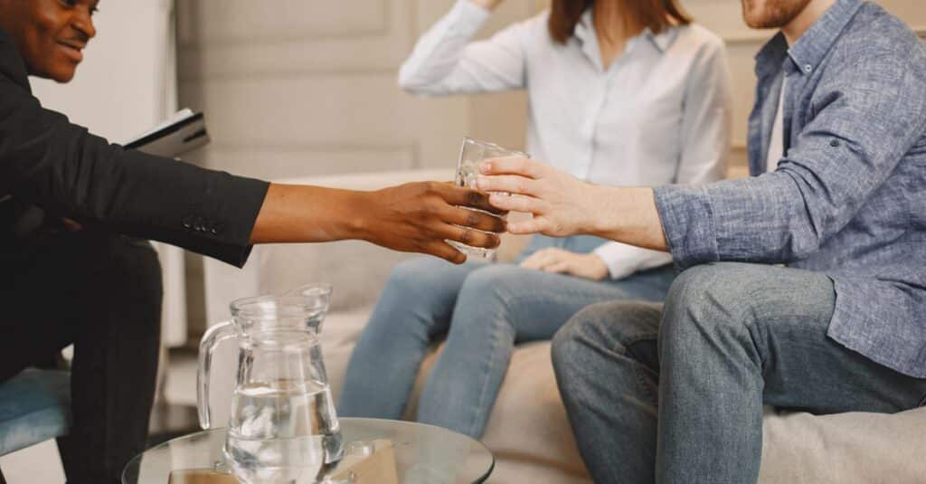 Therapist interacting with couple during counseling session indoors, sharing water.
